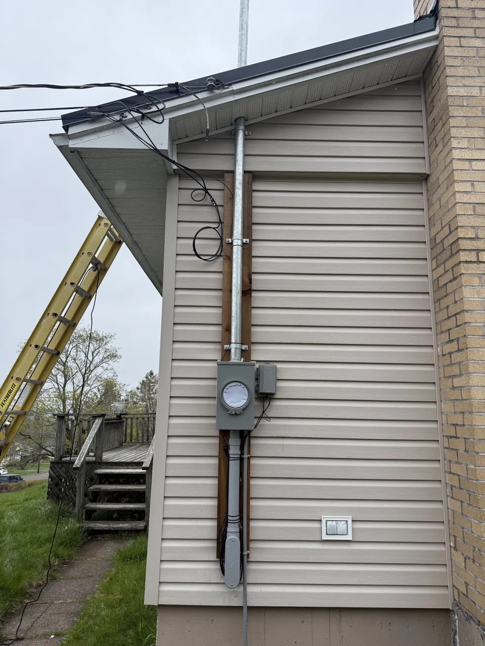 Exterior electrical meter and service mast on a sided house.