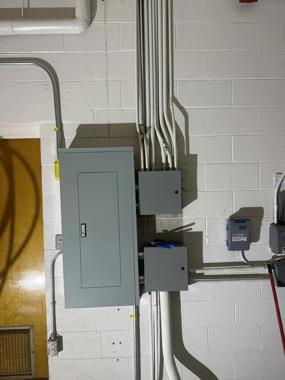 Electrical panel and neatly routed conduits on a painted block wall.