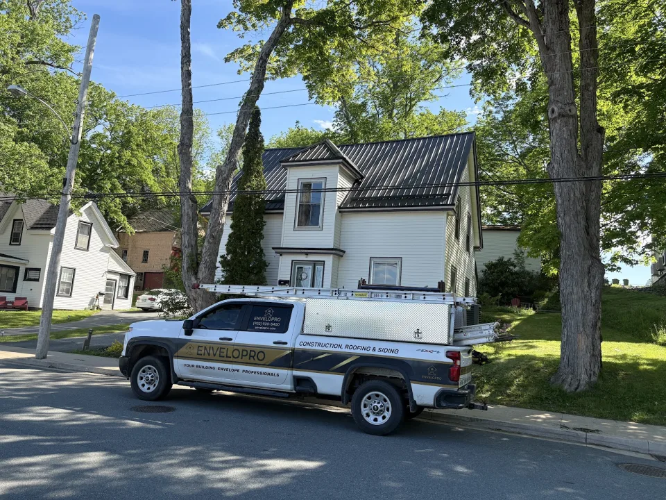 An Envelopro truck outside a house with a dark metal roof.
