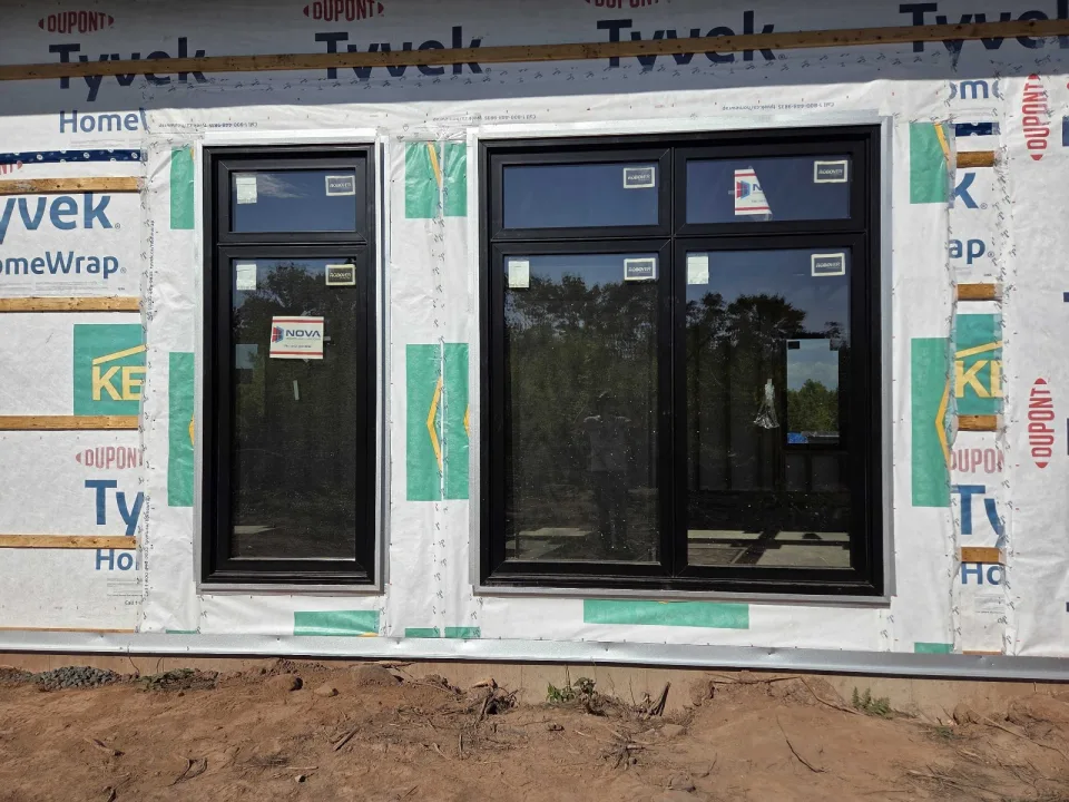 Black-framed windows installed in a wall with building wrap still exposed.